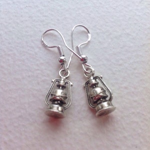 May include: A pair of silver dangle earrings featuring a miniature lantern design. The lanterns have a detailed, antique-style finish.