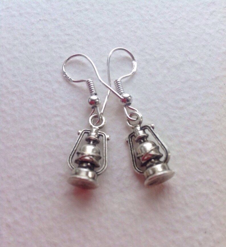 May include: A pair of silver dangle earrings featuring a miniature lantern design. The lanterns have a detailed, antique-style finish.
