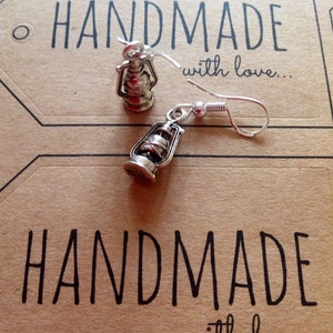 May include: Silver lantern earrings with a hook closure. The earrings are handmade and the card says "Handmade with love..."