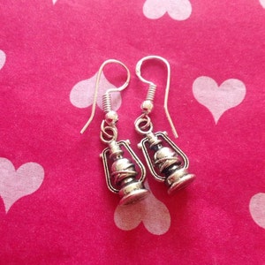 May include: A pair of silver dangle earrings featuring a lantern design. The earrings have a simple hook closure.