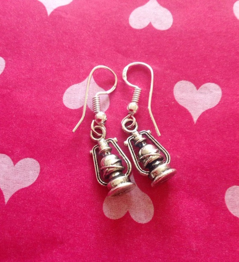May include: A pair of silver dangle earrings featuring a lantern design. The earrings have a simple hook closure.