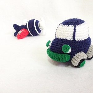 May include: Handmade crochet toy car and airplane. The car is navy blue with white windows, green details, and grey wheels. The airplane is navy blue with white stripes, a red wing, and a white propeller.
