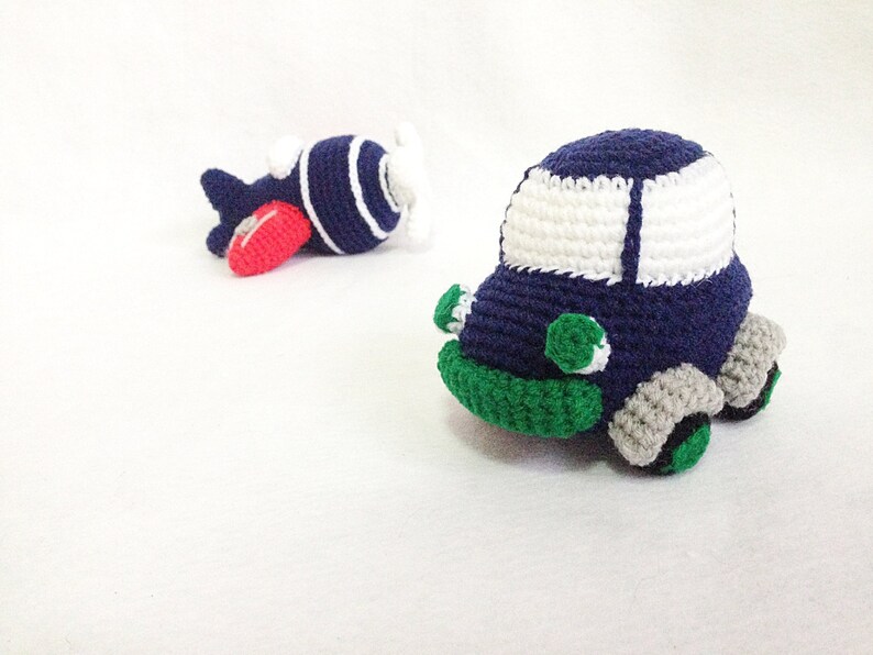 May include: Handmade crochet toy car and airplane. The car is navy blue with white windows, green details, and grey wheels. The airplane is navy blue with white stripes, a red wing, and a white propeller.