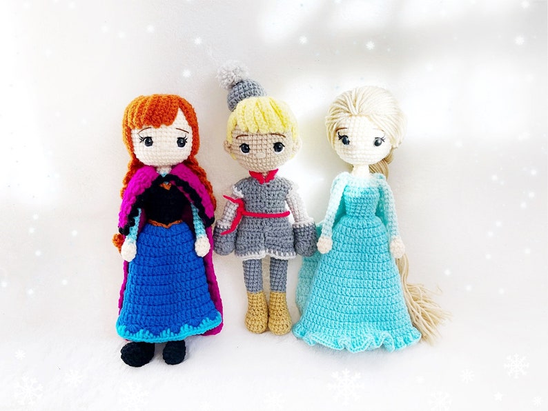 May include: Three crocheted dolls, one with red hair and a blue dress, one with blonde hair and a grey dress, and one with blonde hair and a light blue dress.