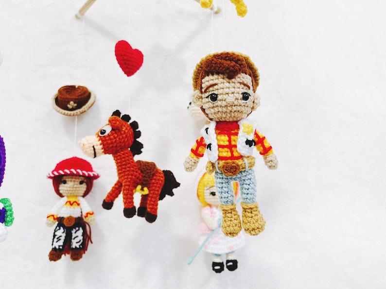 Puede incluir: Un m&oacute;vil de crochet con personajes de la pel&iacute;cula Toy Story. El m&oacute;vil incluye a Woody, Jessie, Bullseye y un coraz&oacute;n. Los personajes est&aacute;n hechos de hilo y tienen detalles bordados.
