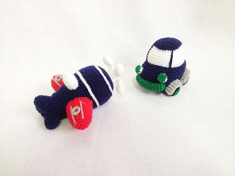 May include: Two handmade crochet toys: a navy blue airplane with red wings and a white propeller, and a navy blue car with a white roof and green and grey accents. The toys are designed for children.