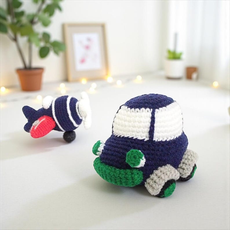 May include: Two handmade crochet toys: a navy blue and white airplane with a red wing and a white propeller, and a navy blue car with white roof, green bumper, and grey wheels. The toys are on a white surface.