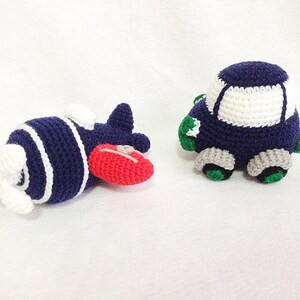 May include: Handmade crocheted toy airplane and car. The airplane is navy blue with white stripes and a red nose. The car is navy blue with a white roof, grey wheels, and green details. Both toys are made from yarn.