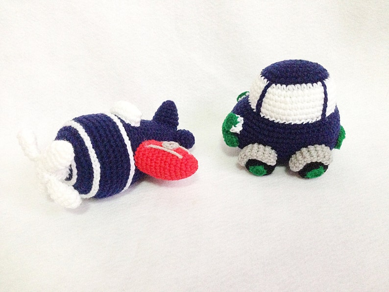 May include: Handmade crocheted toy airplane and car. The airplane is navy blue with white stripes and a red nose. The car is navy blue with a white roof, grey wheels, and green details. Both toys are made from yarn.