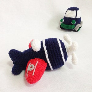 May include: Crocheted airplane and car toys. The airplane is navy blue with white stripes and red wings. The car is navy blue with a white roof and green and grey accents. These handmade toys are perfect for children.
