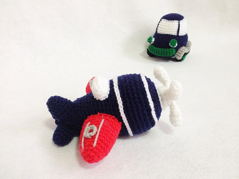 May include: Crocheted airplane and car toys. The airplane is navy blue with white stripes and red wings. The car is navy blue with a white roof and green and grey accents. These handmade toys are perfect for children.