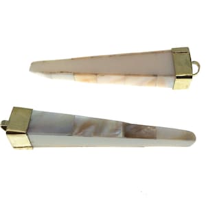 Puede incluir: Dos colgantes de concha blanca y dorada. Cada colgante es largo, delgado y puntiagudo, con una tapa dorada en un extremo. La concha está hecha de pequeñas piezas iridiscentes.