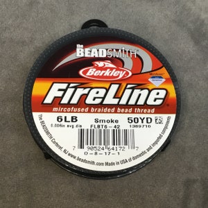 May include: A spool of black FireLine microfused braided bead thread by Berkley. The spool is labeled with the text "6LB 0.006in avg.dia Smoke FLBT6-42 50YD 1389710". The spool is made in the USA of domestic and imported components.