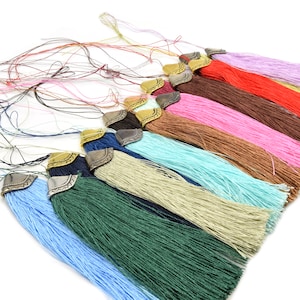 May include: A collection of colorful tassels with decorative metal caps. The tassels are in various colors, including blue, green, pink, and brown. The tassels are made of a silky material and are arranged in a fan shape.