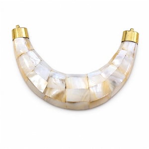 May include: A crescent-shaped pendant featuring a mosaic of iridescent white and cream mother-of-pearl tiles. The curved piece is capped at both ends with polished gold-tone metal hardware, each featuring a small loop for attachment to a chain.