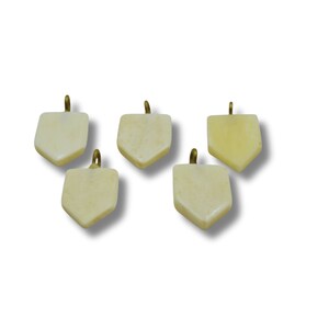 Op de afbeelding: Vijf gebroken witte, beenachtige hangers met een messing lus aan de bovenkant. Elke hanger heeft de vorm van een afgeronde, licht puntige rechthoek.