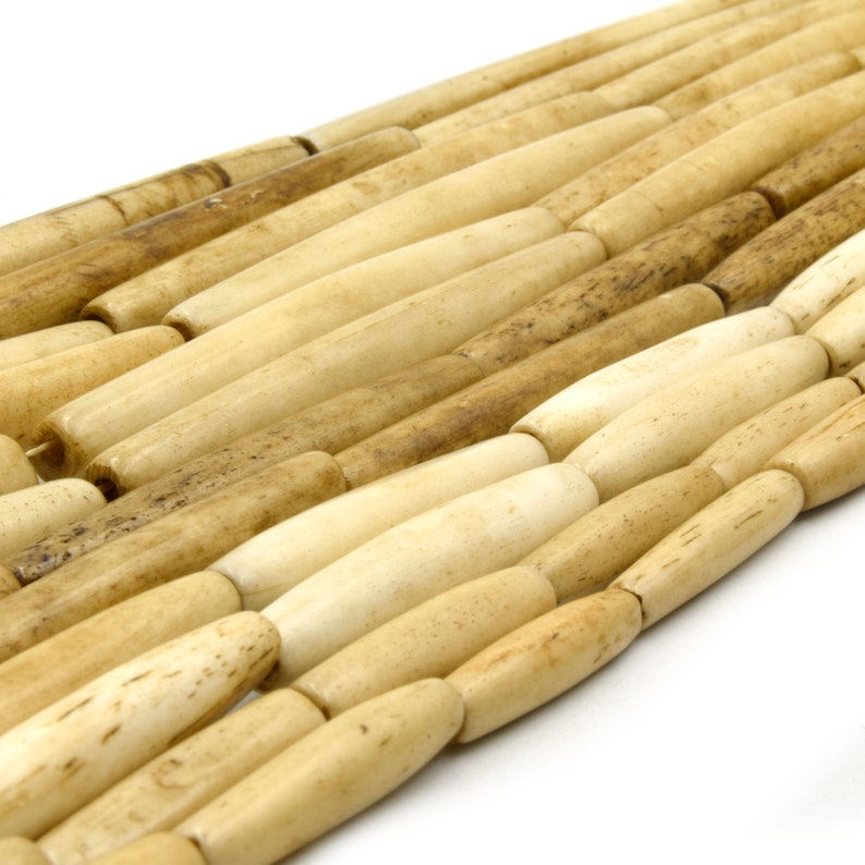Pu&ograve; includere: Una collana di perline in osso naturale, ogni perlina &egrave; di colore beige chiaro con segni marroni. Le perline sono di forma ovale e hanno una finitura liscia e lucida.