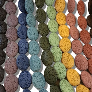 May include: A close-up of a strand of lava rock beads. The beads are oval-shaped and have a rough, textured surface. The beads are a variety of colors, including brown, gray, green, and black.