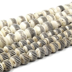 May include: A strand of white bone beads with black carved lines. The beads are round and have a slightly irregular shape.