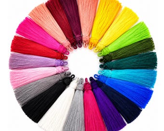Könnte beinhalten: Eine kreisförmige Anordnung zahlreicher seidenartiger Quasten in einem breiten Farbspektrum, darunter Rot, Pink, Orange, Gelb, Grün, Blau, Violett, Schwarz, Weiß und Grau. Jede Quaste hat oben eine Schlaufe zur Befestigung.