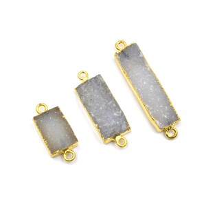 May include: Three rectangular gemstone connectors with a gold-colored border and loops. The gemstones have a gray, crystalline appearance. The connectors are arranged on a white background.