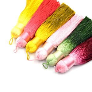 May include: Assortment of colorful silk tassels with a gradient of colors, including yellow, pink, green, and red. The tassels are tied together and have a loop at the top for hanging.