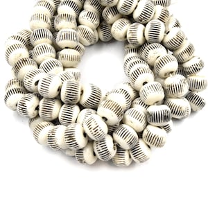 May include: A strand of white ceramic beads with black stripes. The beads are round and have a slightly textured surface.
