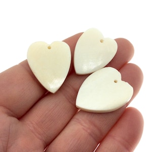 May include: Three white heart-shaped pendants with a hole for stringing. The pendants are made of bone and have a smooth, polished finish.