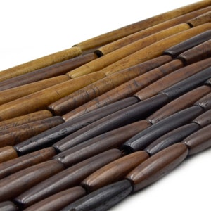 Pu&ograve; includere: Primo piano di una collana di perline di legno marroni, nere e beige. Le perline sono lunghe e cilindriche e sono disposte in uno schema sfalsato.