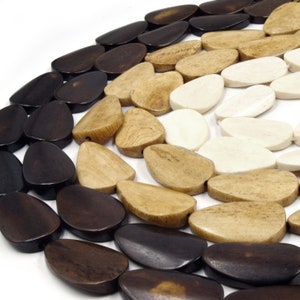 May include: A close-up of a collection of wooden beads in various shades of brown, beige, and white. The beads are oval-shaped and have a smooth, polished finish.