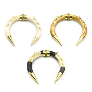 May include: Three crescent-shaped horn pendants with gold accents. The horns are made of bone and have a natural, polished finish. The gold accents are in the form of small, round studs and a band around the centre of each horn.