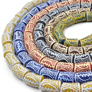 Puede incluir: Primer plano de un conjunto de cuentas coloridas y estampadas. Las cuentas están hechas de madera y tienen una variedad de diseños geométricos. Las cuentas están enhebradas en una larga hebra, y los colores son brillantes y vibrantes.