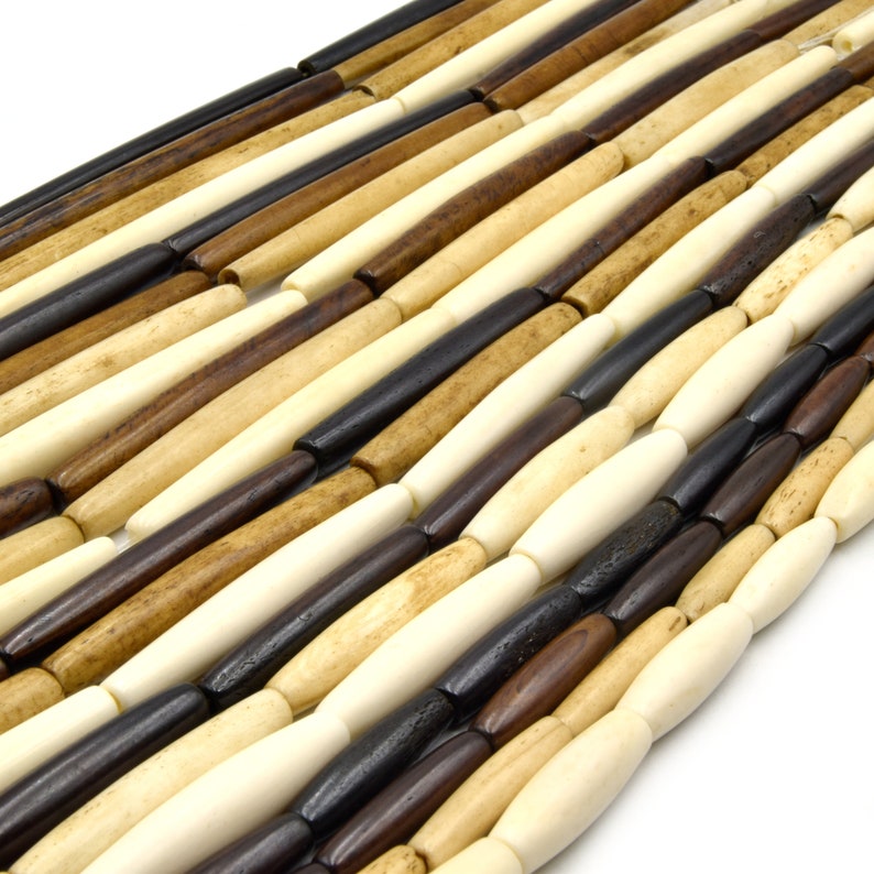 Pu&ograve; includere: Una collana di perline di legno in varie tonalit&agrave; di marrone, beige e nero. Le perline sono cilindriche e hanno una finitura liscia e lucida.