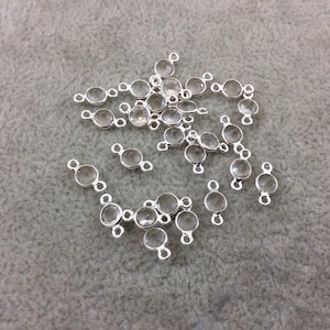 Op de afbeelding: Een verzameling van heldere kristallen kralen met zilveren springringen. De kralen zijn rond en hebben een gladde, gepolijste afwerking. De springringen zijn aan de kralen bevestigd en maken het gemakkelijk om ze aan elkaar te rijgen.