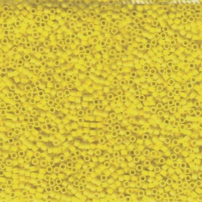 Pu&ograve; includere: Primo piano di un mucchio di piccole perline cilindriche gialle. Ogni perlina ha un foro al centro. Le perline sono di dimensioni e forma uniformi e sono fittamente impacchettate, creando una superficie strutturata.