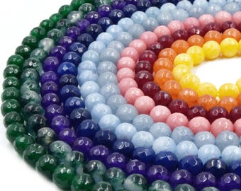 May include: A collection of round, faceted gemstone beads arranged in a circular gradient pattern. The beads display a spectrum of colors including deep green, purple, light blue, pink, orange, and yellow, all featuring a polished finish.