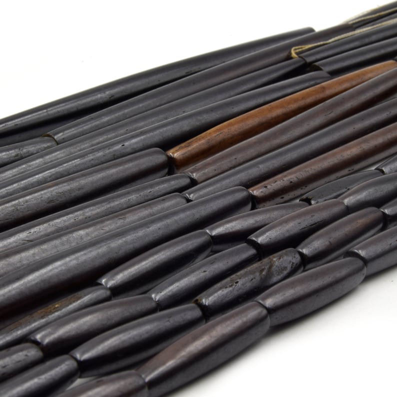 Pu&ograve; includere: Una collana di perline di legno nere e marroni. Le perline sono lunghe e cilindriche con estremit&agrave; arrotondate. Le perline sono disposte a spina di pesce.