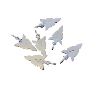 Könnte beinhalten: Sechs silberne Pfeilspitzen-Anhänger mit strukturierter Oberfläche. Die Pfeilspitzen sind auf einem weißen Hintergrund verstreut.