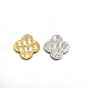 Puede incluir: Dos dijes en forma de tr&eacute;bol, uno dorado y otro plateado, ambos cubiertos de brillantes piedras de imitaci&oacute;n.