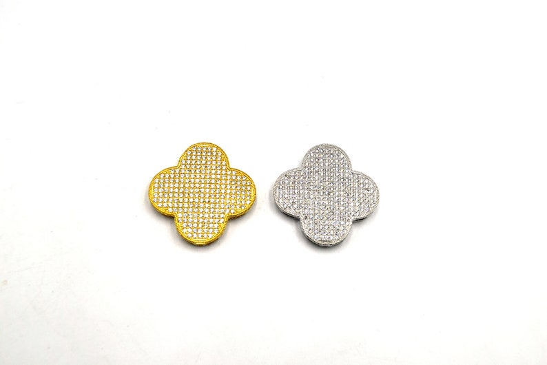 Puede incluir: Dos dijes en forma de tr&eacute;bol, uno dorado y otro plateado, ambos cubiertos de brillantes piedras de imitaci&oacute;n.