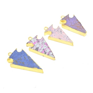 May include: Four gemstone arrow pendants with gold-colored trim. The pendants feature a variety of colors, including blue, pink, and purple, with a speckled pattern. Each pendant has a small loop at the top for attaching to a chain or cord.