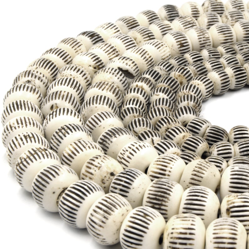 May include: A strand of white and black beads with a striped pattern. The beads are round and have a slightly rough texture.