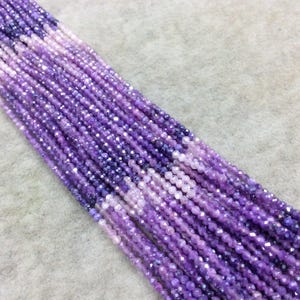 May include: Strands of faceted beads in varying shades of purple, from deep violet to pale lavender. The beads are small and strung together, creating a shimmering effect. The beads are likely for jewelry making.
