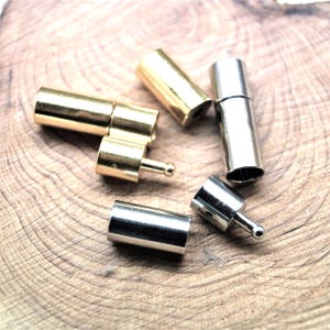 Op de afbeelding: Een verzameling cilindrische metalen sieradensluitingen in goud- en zilverkleurige tinten. De set bevat verschillende tonvormige onderdelen, sommige met een klein uitstekend pinmechanisme voor een veilige bevestiging, met gladde, gepolijste metalen oppervlakken.