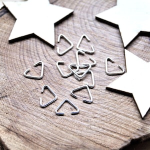May include: A collection of small, silver-coloured metal triangle-shaped jump rings. Each piece is formed from a thin wire bent into an open triangular frame, featuring a smooth, metallic finish and a consistent, uniform size across all items.