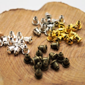 Peut inclure: Assortiment de dos d'oreille en métal argenté, doré et bronze. Les dos sont petits et ronds avec un dessus plat.