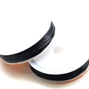 May include: Two spools of black beading wire are shown against a white backdrop. The wire is tightly wound on white spools. The wire appears to be a thin, flexible material, suitable for jewellery making or crafts.