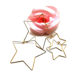 May include: Three gold star-shaped hoops of different sizes. The largest hoop is partially obscured by a pink flower.