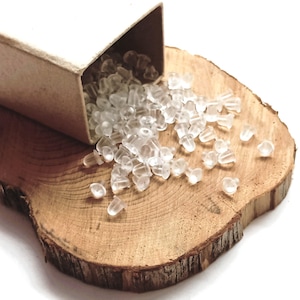 Peut inclure: Des dos de boucles d'oreilles transparents et clairs, déversés d'une petite boîte en carton ouverte sur une surface en bois rustique. Les dos de boucles d'oreilles sont petits, en forme de champignon. Le bois est brun clair avec un grain visible.