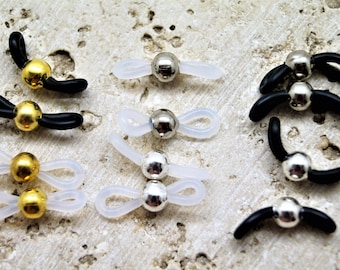 May include: An assortment of eyeglass retainers in various styles. The retainers feature small, metallic spheres in gold and silver tones, attached to black or clear rubber loops designed to secure glasses.
